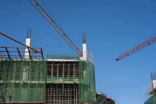 Crane and building construction site against blue sky. Metal construction of unfinished building on construction. Tower Crane use for building of multi storage building