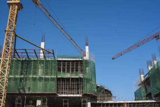 Crane and building construction site against blue sky. Metal construction of unfinished building on construction. Tower Crane use for building of multi storage building