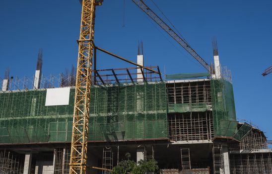 Crane and building construction site against blue sky. Metal construction of unfinished building on construction. Tower Crane use for building of multi storage building