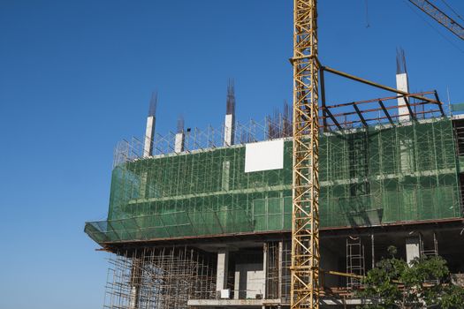 Crane and building construction site against blue sky. Metal construction of unfinished building on construction. Tower Crane use for building of multi storage building