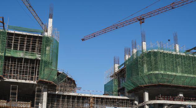 Crane and building construction site against blue sky. Metal construction of unfinished building on construction. Tower Crane use for building of multi storage building