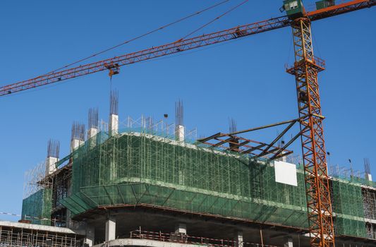 Crane and building construction site against blue sky. Metal construction of unfinished building on construction. Tower Crane use for building of multi storage building