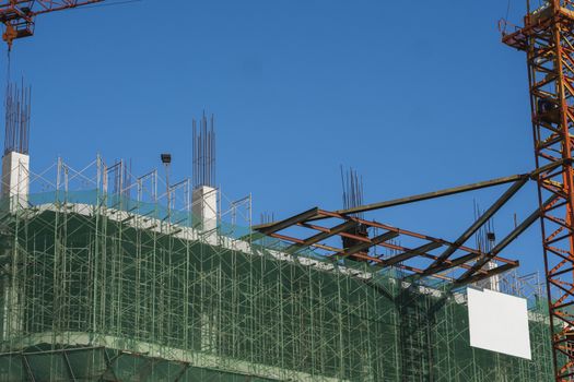 Crane and building construction site against blue sky. Metal construction of unfinished building on construction. Tower Crane use for building of multi storage building