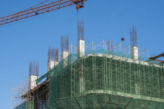 Crane and building construction site against blue sky. Metal construction of unfinished building on construction. Tower Crane use for building of multi storage building