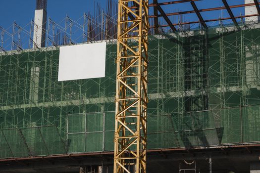 Crane and building construction site against blue sky. Metal construction of unfinished building on construction. Tower Crane use for building of multi storage building