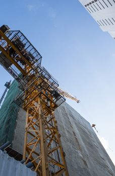 Crane and building construction site against blue sky. Metal construction of unfinished building on construction. Tower Crane use for building of multi storage building