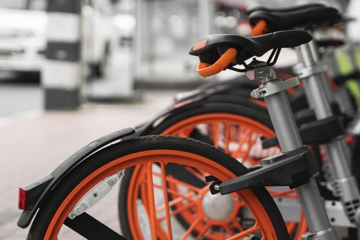 Street transportation orange hybrid rent bicycles with electronic form of payment for traveling around the city stand in row