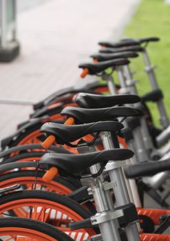 Street transportation orange hybrid rent bicycles with electronic form of payment for traveling around the city stand in row