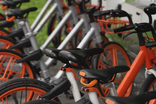 Street transportation orange hybrid rent bicycles with electronic form of payment for traveling around the city stand in row