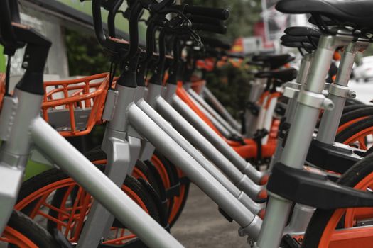 Street transportation orange hybrid rent bicycles with electronic form of payment for traveling around the city stand in row