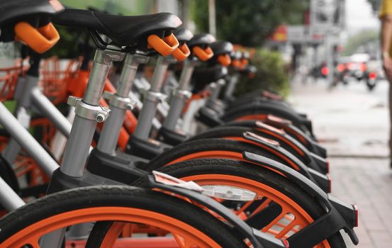 Street transportation orange hybrid rent bicycles with electronic form of payment for traveling around the city stand in row