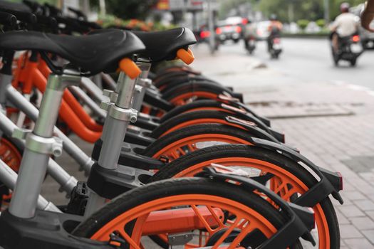 Street transportation orange hybrid rent bicycles with electronic form of payment for traveling around the city stand in row