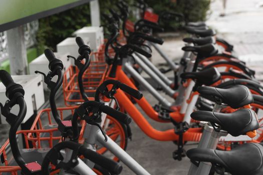 Street transportation orange hybrid rent bicycles with electronic form of payment for traveling around the city stand in row