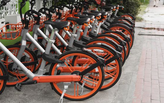 Street transportation orange hybrid rent bicycles with electronic form of payment for traveling around the city stand in row