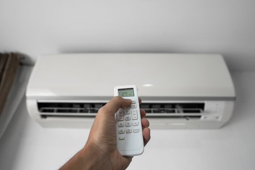 Man's hand using remote controler. Hand holding rc and adjusting temperature of air conditioner mounted on a white wall. Indooor comfort temperature. Health concepts and energy savings