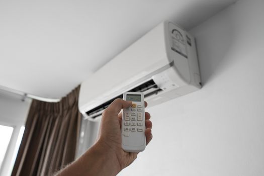 Man's hand using remote controler. Hand holding rc and adjusting temperature of air conditioner mounted on a white wall. Indooor comfort temperature. Health concepts and energy savings