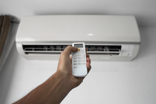 Man's hand using remote controler. Hand holding rc and adjusting temperature of air conditioner mounted on a white wall. Indooor comfort temperature. Health concepts and energy savings