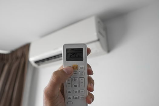 Man's hand using remote controler. Hand holding rc and adjusting temperature of air conditioner mounted on a white wall. Indooor comfort temperature. Health concepts and energy savings