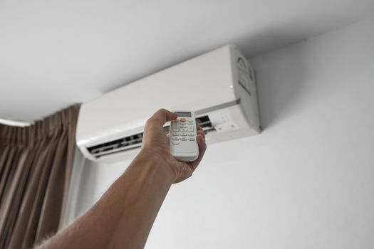 Man's hand using remote controler. Hand holding rc and adjusting temperature of air conditioner mounted on a white wall. Indooor comfort temperature. Health concepts and energy savings