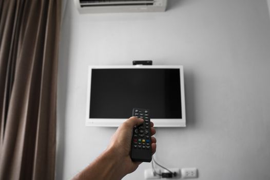 The man with the remote control in hand want switch on the TV and presses the button on the remote control. Remote control in hand closeup