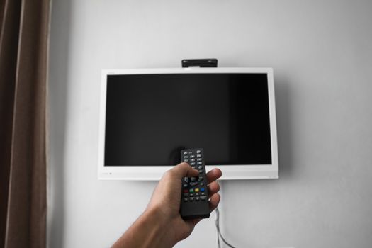 The man with the remote control in hand want switch on the TV and presses the button on the remote control. Remote control in hand closeup