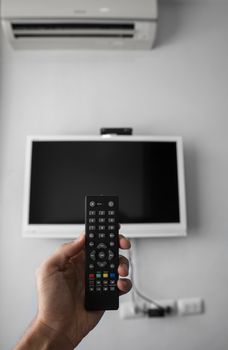 The man with the remote control in hand want switch on the TV and presses the button on the remote control. Remote control in hand closeup