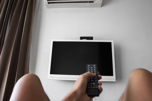 The man with the remote control in hand want switch on the TV and presses the button on the remote control. Remote control in hand closeup