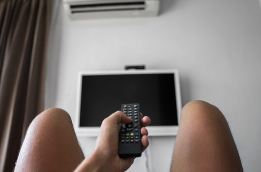 The man with the remote control in hand want switch on the TV and presses the button on the remote control. Remote control in hand closeup