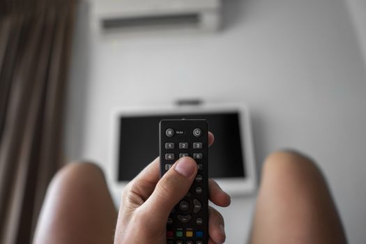The man with the remote control in hand want switch on the TV and presses the button on the remote control. Remote control in hand closeup