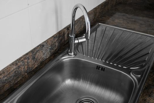 Close up on modern kitchen metal faucet and metal kitchen sink