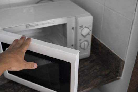 Man hand holdind a door of microwave in a kitchen for cooking or heating a dish