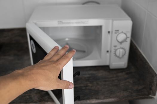 Man hand holdind a door of microwave in a kitchen for cooking or heating a dish