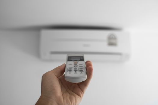 Man's hand using remote controler. Hand holding rc and adjusting temperature of air conditioner mounted on a white wall. Indooor comfort temperature. Health concepts and energy savings