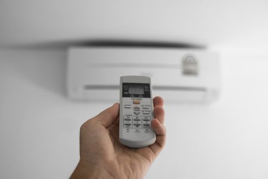 Man's hand using remote controler. Hand holding rc and adjusting temperature of air conditioner mounted on a white wall. Indooor comfort temperature. Health concepts and energy savings