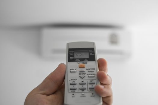 Man's hand using remote controler. Hand holding rc and adjusting temperature of air conditioner mounted on a white wall. Indooor comfort temperature. Health concepts and energy savings