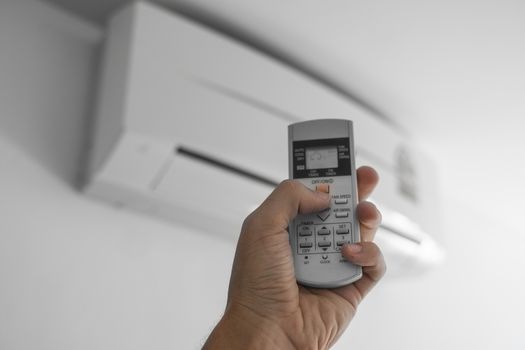 Man's hand using remote controler. Hand holding rc and adjusting temperature of air conditioner mounted on a white wall. Indooor comfort temperature. Health concepts and energy savings