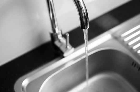 Close up on modern kitchen metal faucet and metal kitchen sink with a running water
