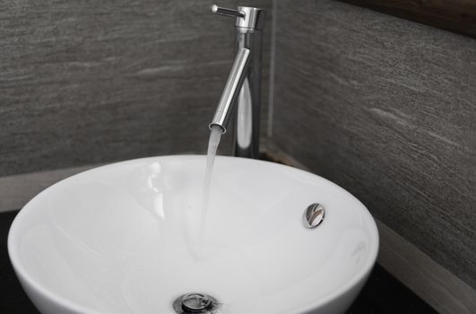 Bathroom interior with white round sink and chrome faucet in a modern bathroom. Water flowing from the chrome faucet