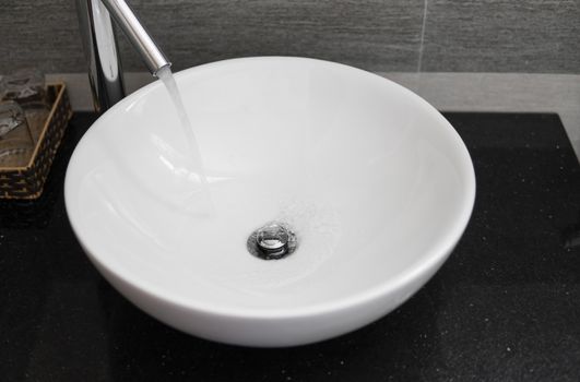 Bathroom interior with white round sink and chrome faucet in a modern bathroom. Water flowing from the chrome faucet