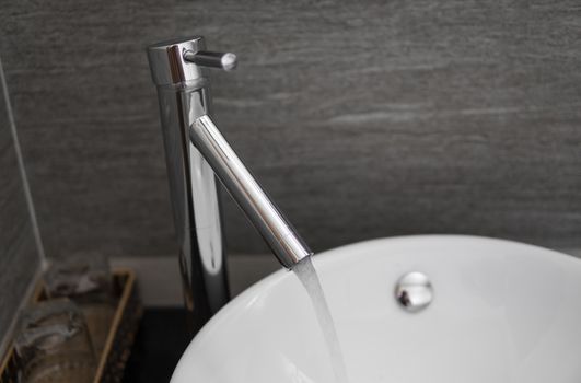 Bathroom interior with white round sink and chrome faucet in a modern bathroom. Water flowing from the chrome faucet