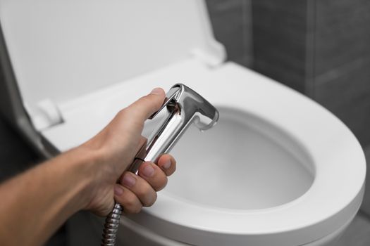 Using of bidet shower with a white toilet. Bidet shower in male hand for using with a white toilet bowl