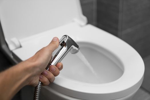 Using of bidet shower with a white toilet. Bidet shower in male hand for using with a white toilet bowl