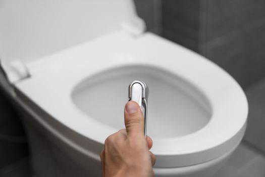 Using of bidet shower with a white toilet. Bidet shower in male hand for using with a white toilet bowl