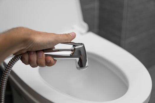 Using of bidet shower with a white toilet. Bidet shower in male hand for using with a white toilet bowl