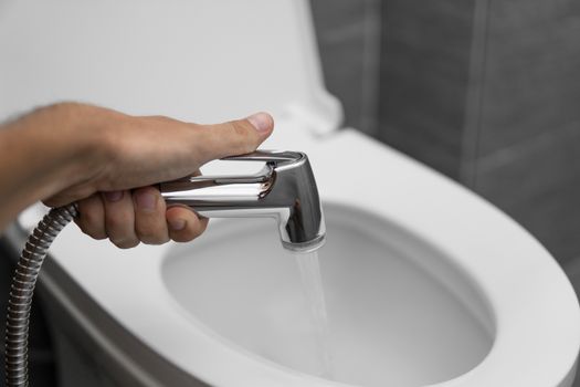 Using of bidet shower with a white toilet. Bidet shower in male hand for using with a white toilet bowl