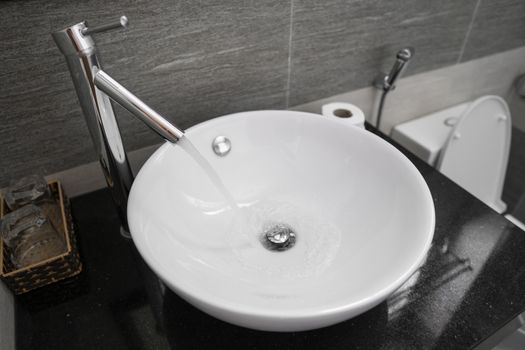 Bathroom interior with white round sink and chrome faucet in a modern bathroom. Water flowing from the chrome faucet