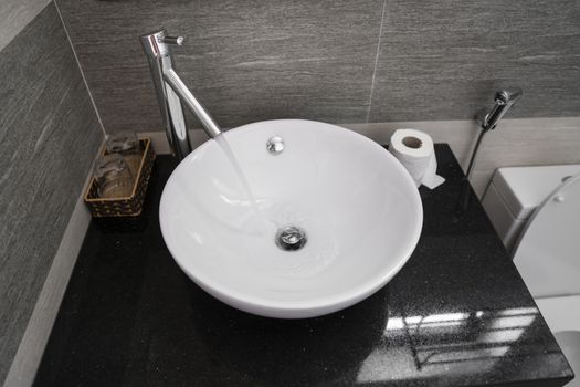 Bathroom interior with white round sink and chrome faucet in a modern bathroom. Water flowing from the chrome faucet