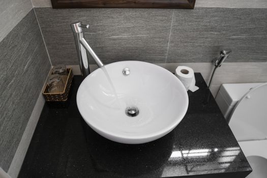 Bathroom interior with white round sink and chrome faucet in a modern bathroom. Water flowing from the chrome faucet