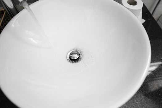 Bathroom interior with white round sink and chrome faucet in a modern bathroom. Water flowing from the chrome faucet