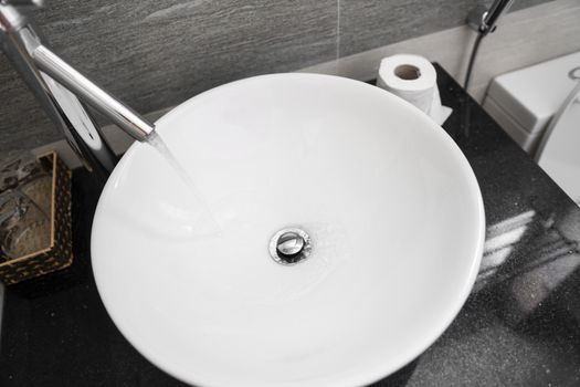 Bathroom interior with white round sink and chrome faucet in a modern bathroom. Water flowing from the chrome faucet